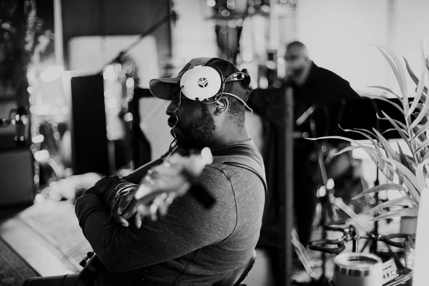 Black and white photo of a man wearing a cap with headphones around his neck in a music studio.
