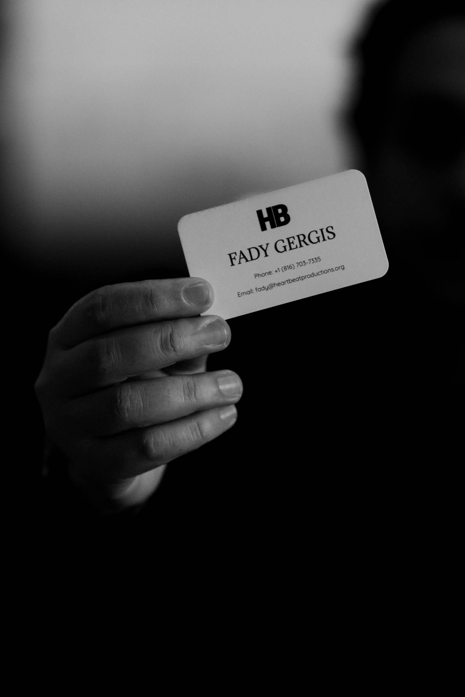 Hand holding a business card for Fady Gergis at HB Heartbeat Productions with contact details.