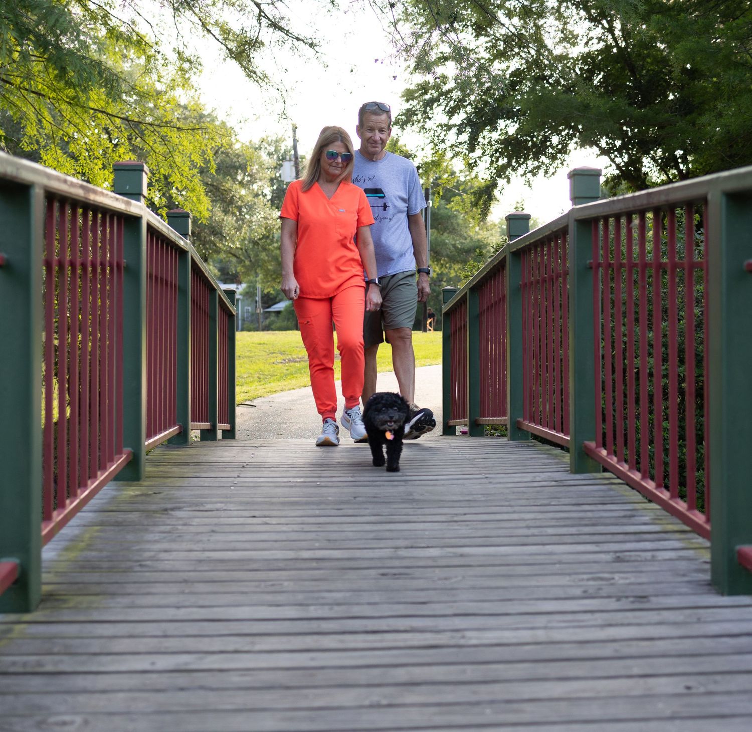Pet parents walking over bridge with small black poodle.