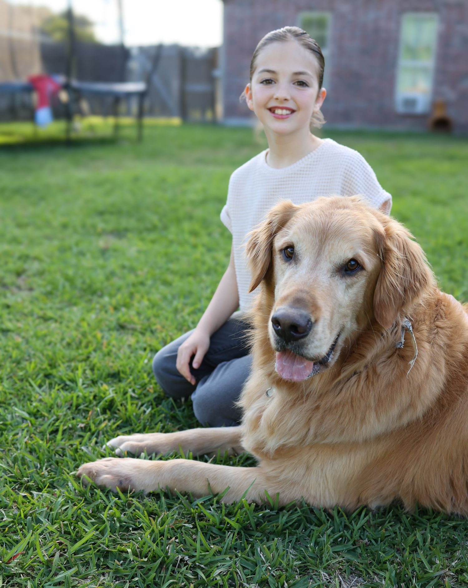Girl sitting next to her golden retriever in the backyard
