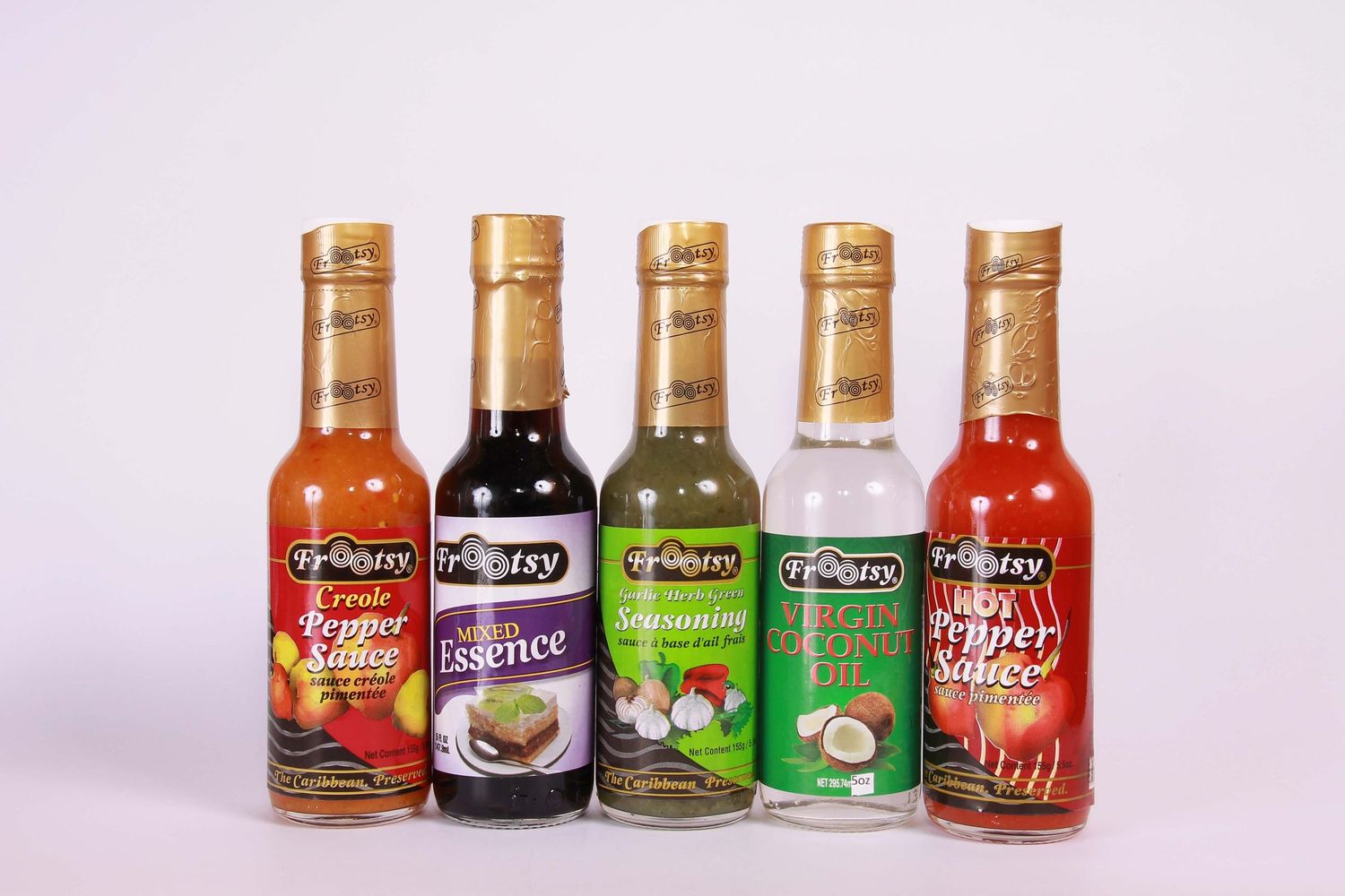 Five Tropitry brand sauce bottles including hot pepper sauce, essence, seasoning, coconut oil, and chili sauce.