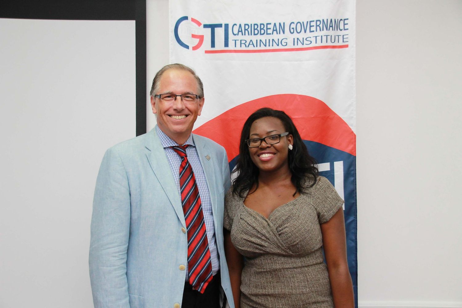 Two professionals posing together at Caribbean Governance Training Institute event banner backdrop.