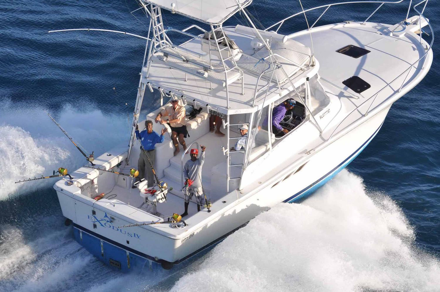 Group of anglers on a white sport fishing boat speeding through blue ocean waters on a sunny day.
