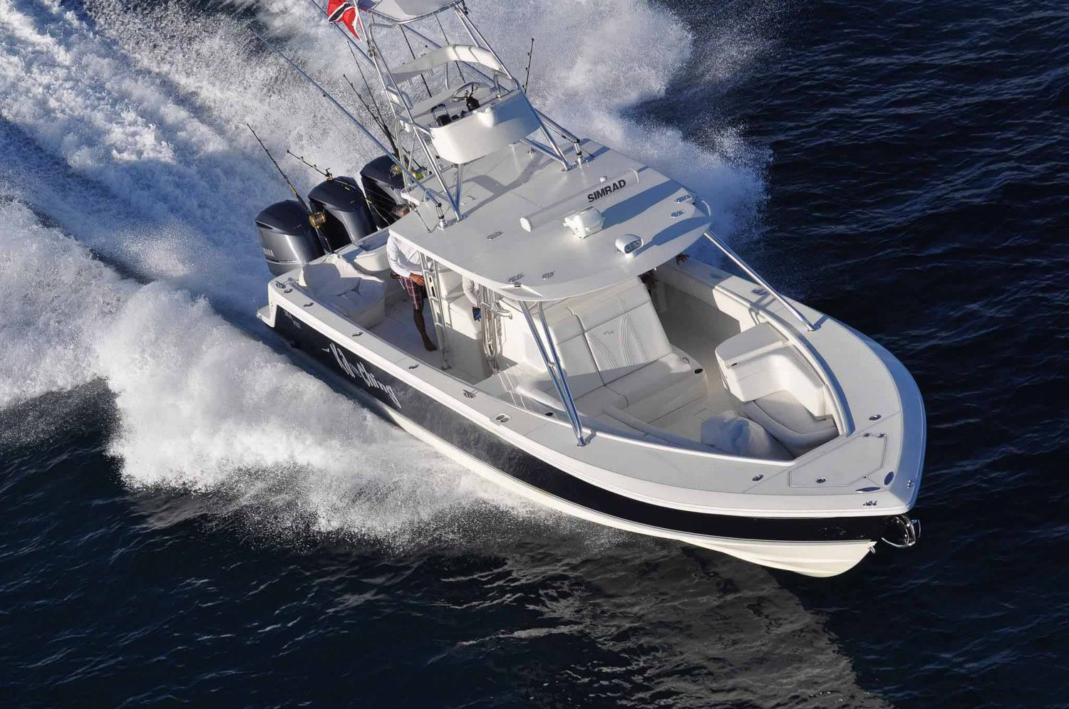 Aerial view of a sleek white motorboat speeding through blue ocean waters, creating large white wake waves.