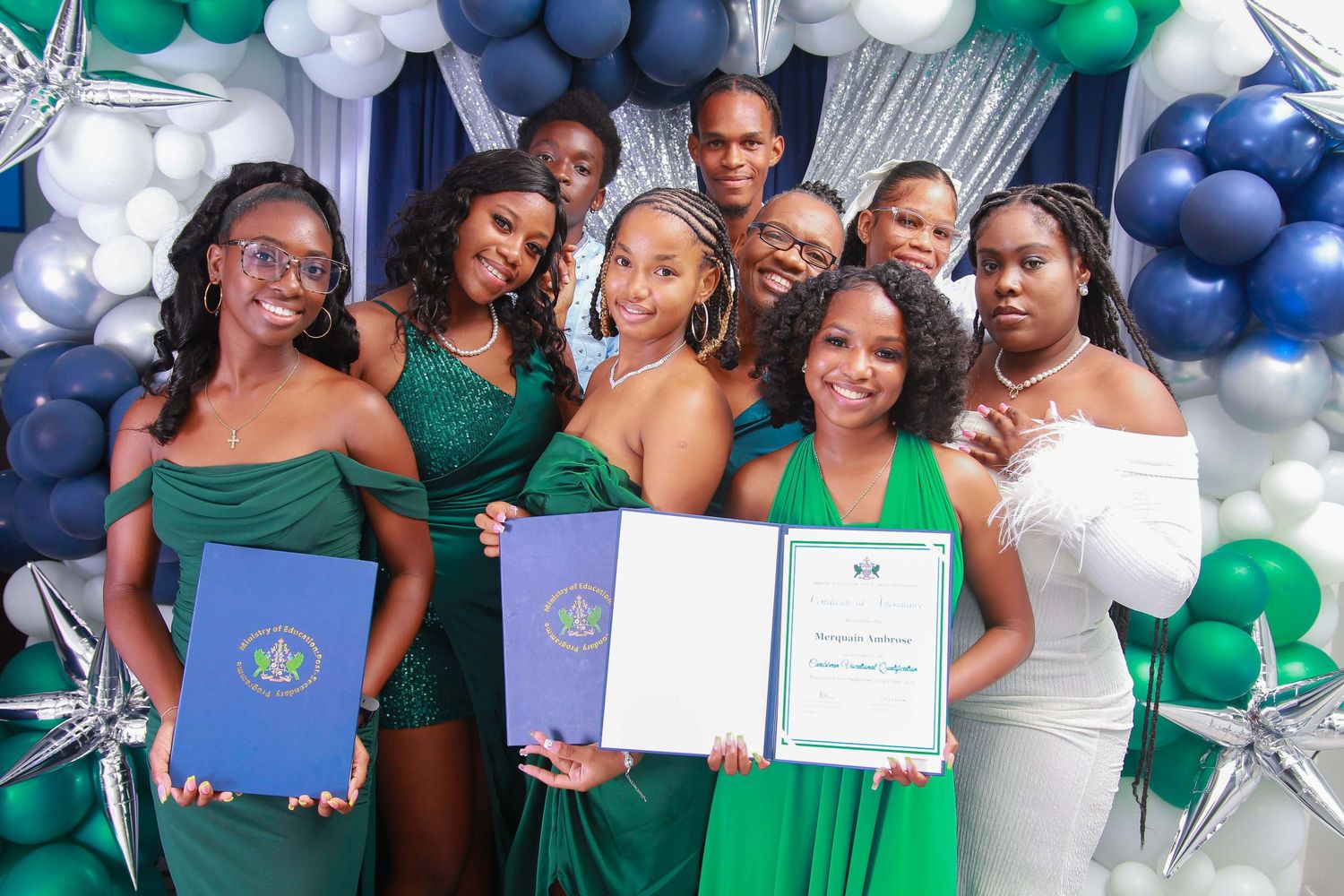 Group of graduates in green dresses celebrating with diplomas and certificates at a formal ceremony.