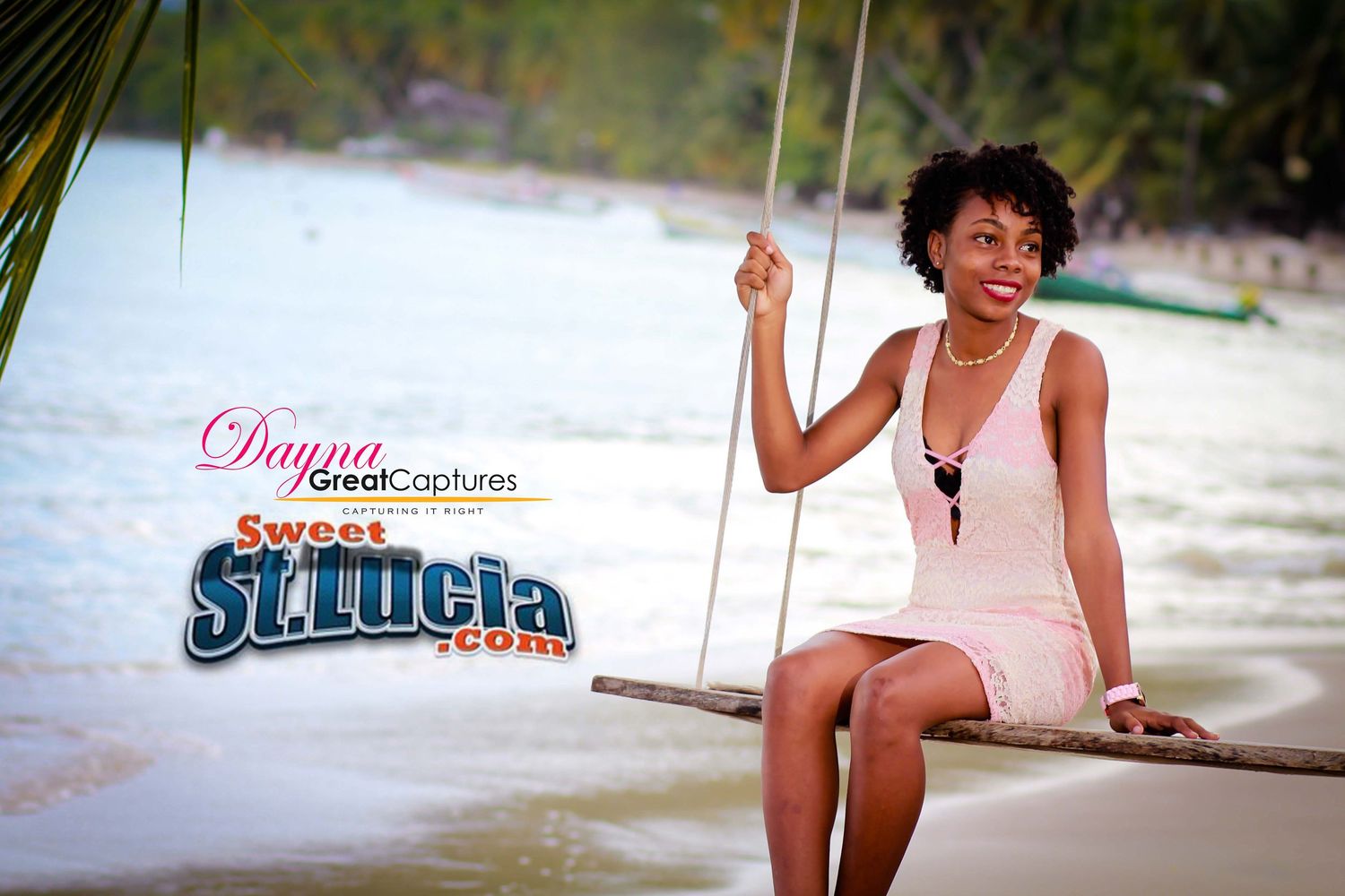 A woman sitting on a rope swing on a tropical beach in St. Lucia, wearing a white dress and pearl necklace.
