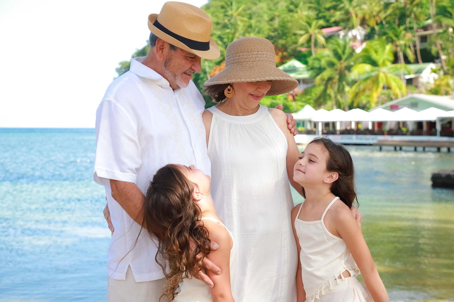 Family in white outfits enjoying a tropical beach vacation, with palm trees and turquoise water in the background.
