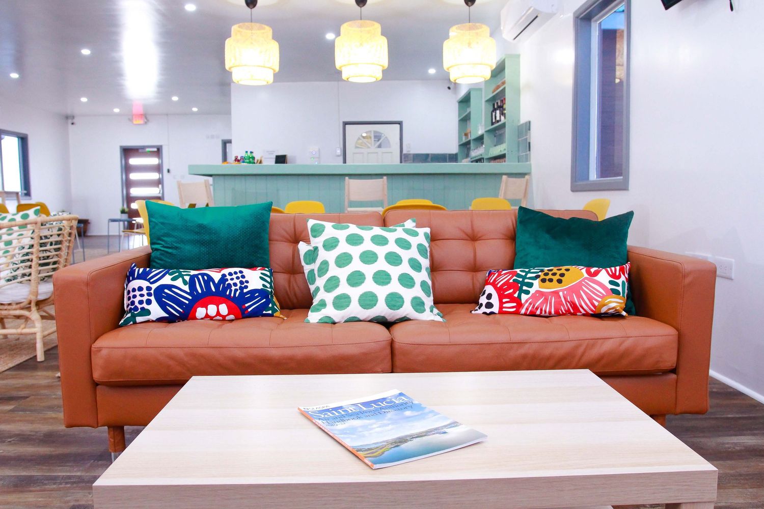 Bright living room with orange leather sofa, colorful throw pillows, wooden coffee table, and pendant lights above.