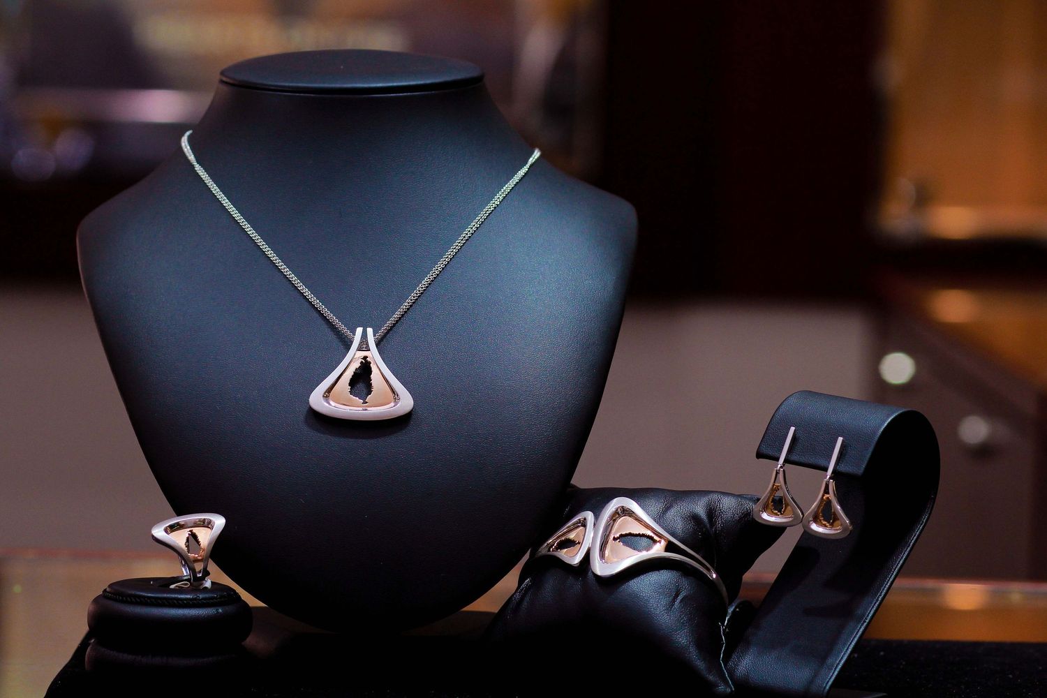 Rose gold triangular pendant necklace, ring, and earrings jewelry set displayed on black velvet stand.