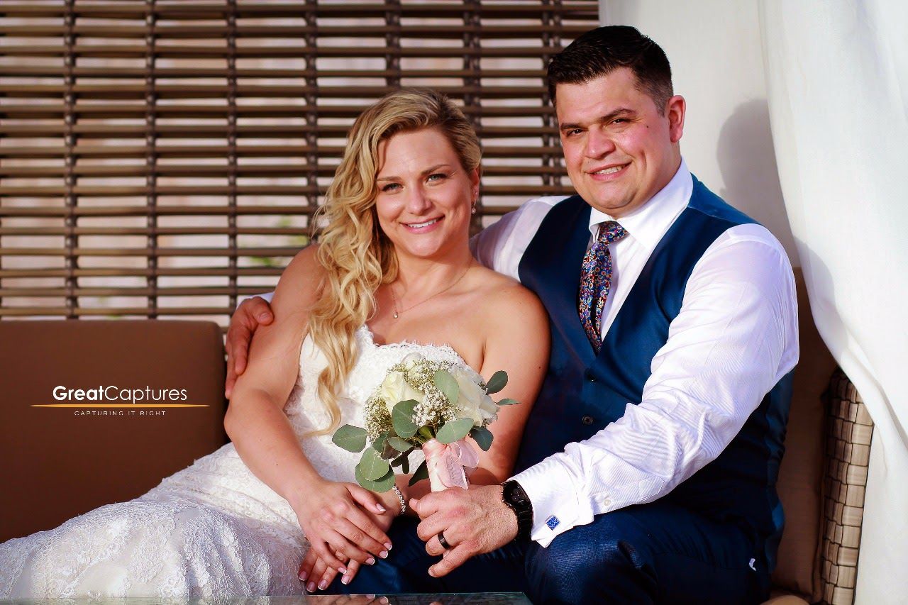 Smiling bride and groom pose together in wedding attire, she holds a bouquet, photographed by Great Captures.