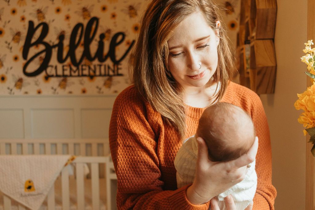 A caregiver in an orange sweater tenderly holds a sleeping baby in a nursery with star-patterned walls.