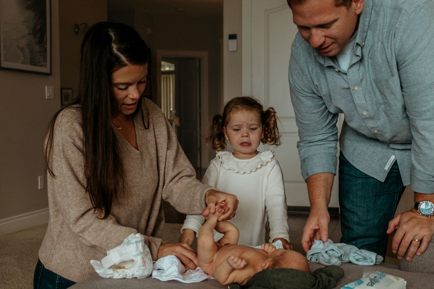 A family changes their baby's diaper together while spending quality time at home.