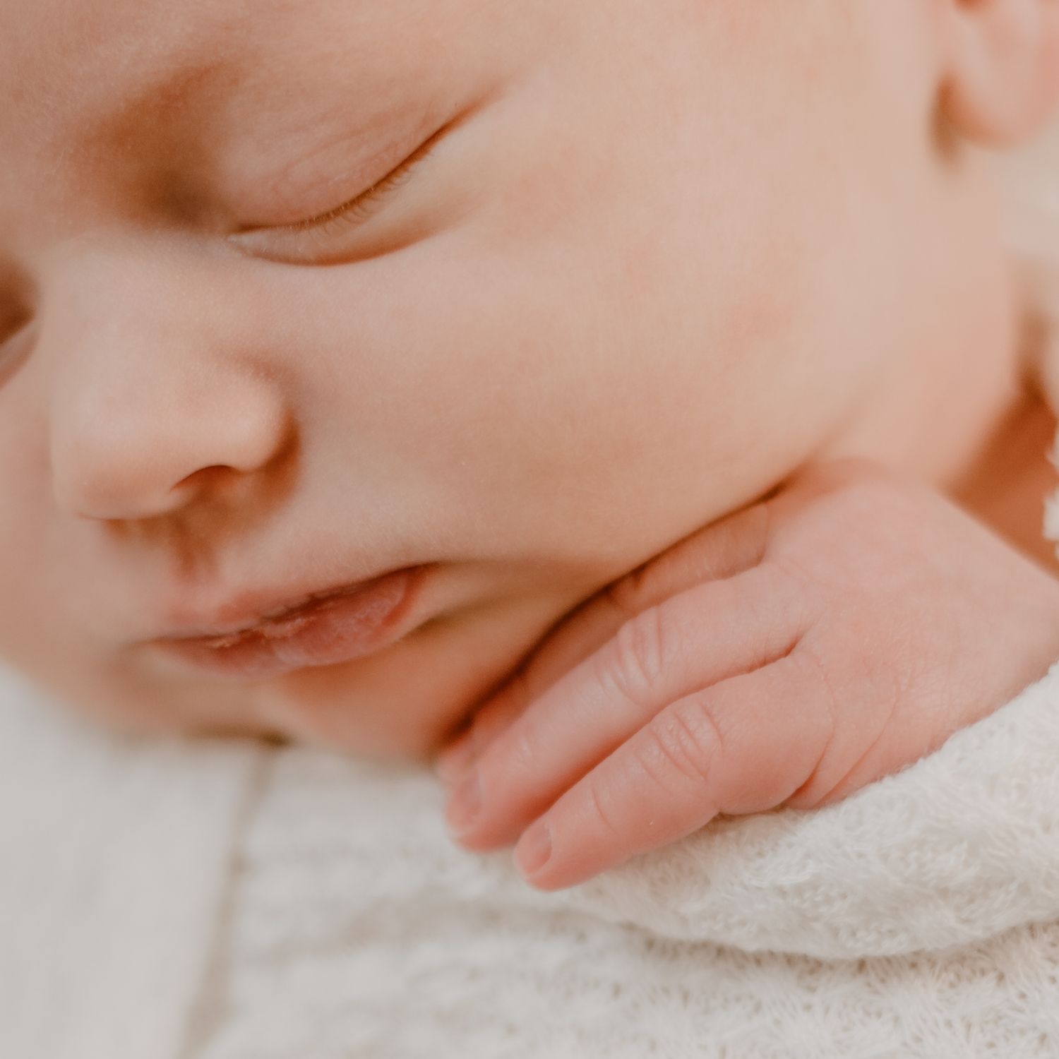 Tiny baby hand reaching out to touch soft white fabric, capturing a gentle moment of exploration and discovery.