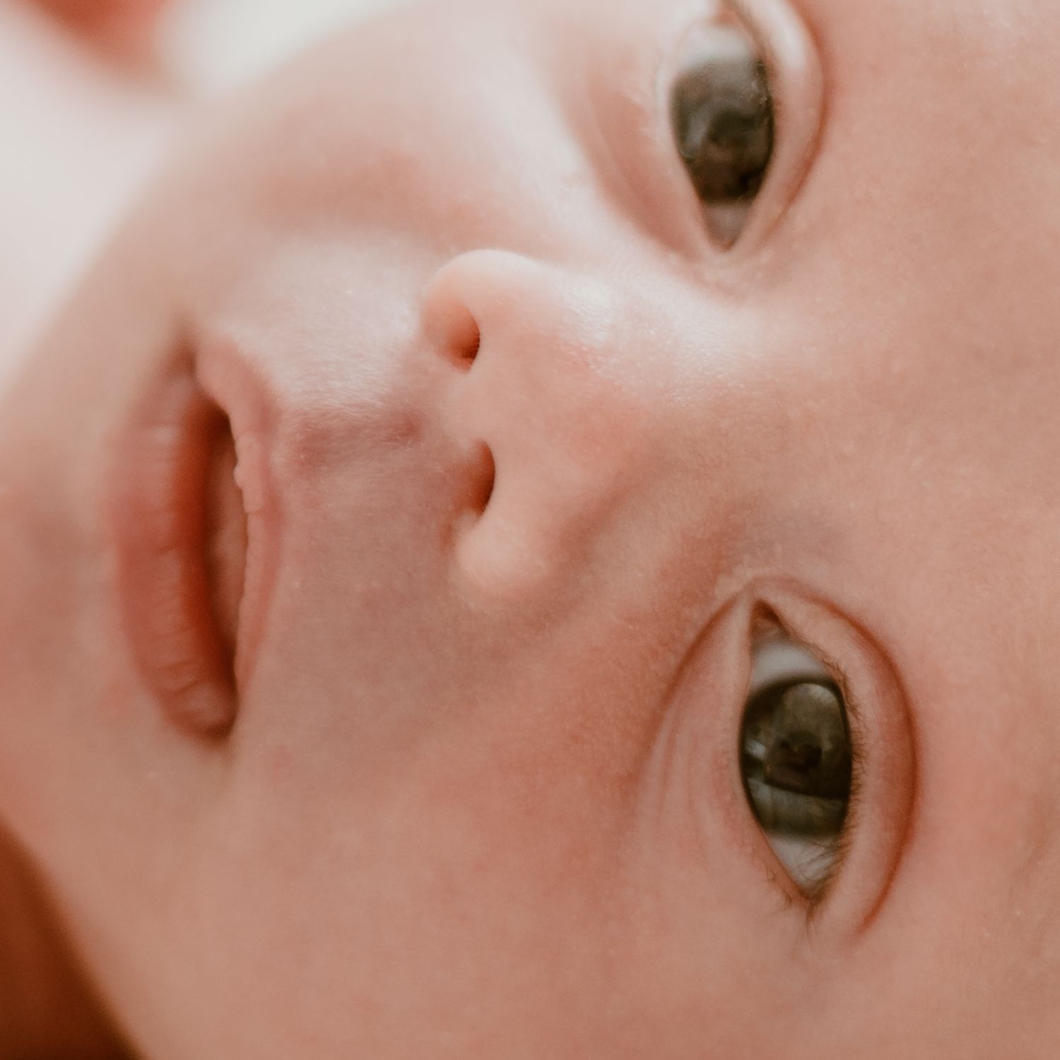 Close up of an infant's face with large expressive brown eyes looking directly at camera.