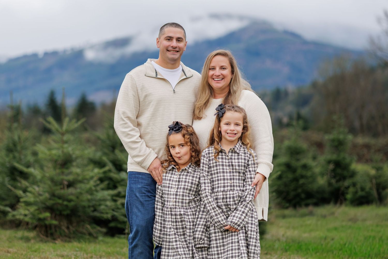 Family poses together in outdoor setting with mountains and evergreen trees in background.
