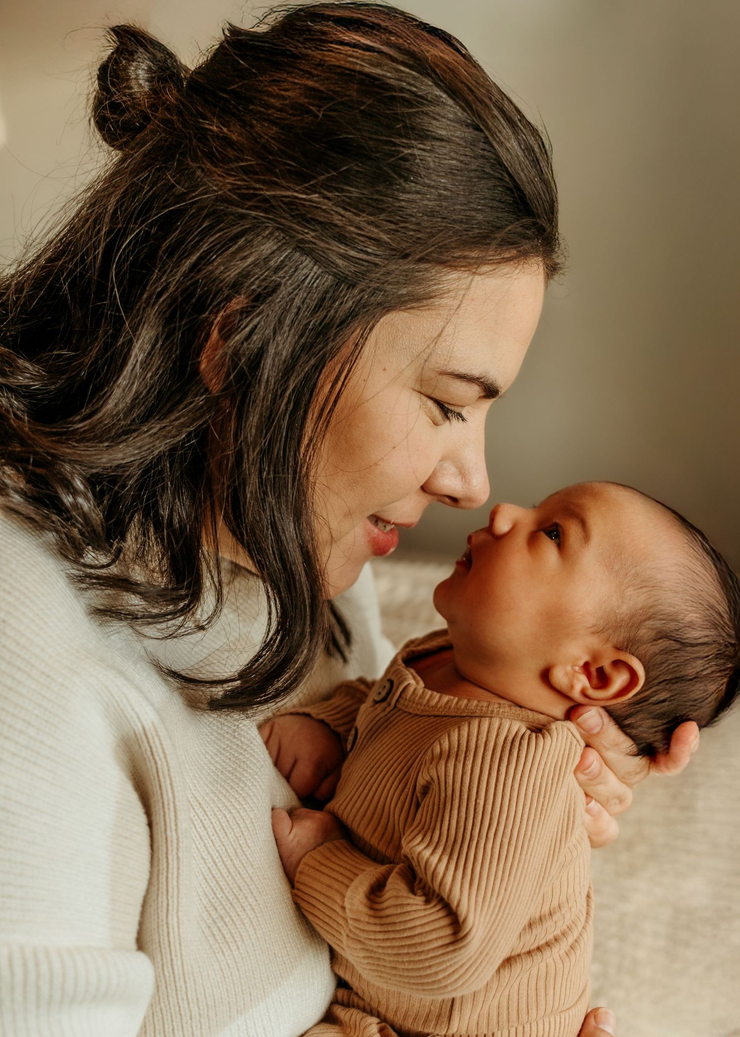 A tender moment captured in a warm-toned series showing gentle affection between mother and baby in cream knit sweaters.