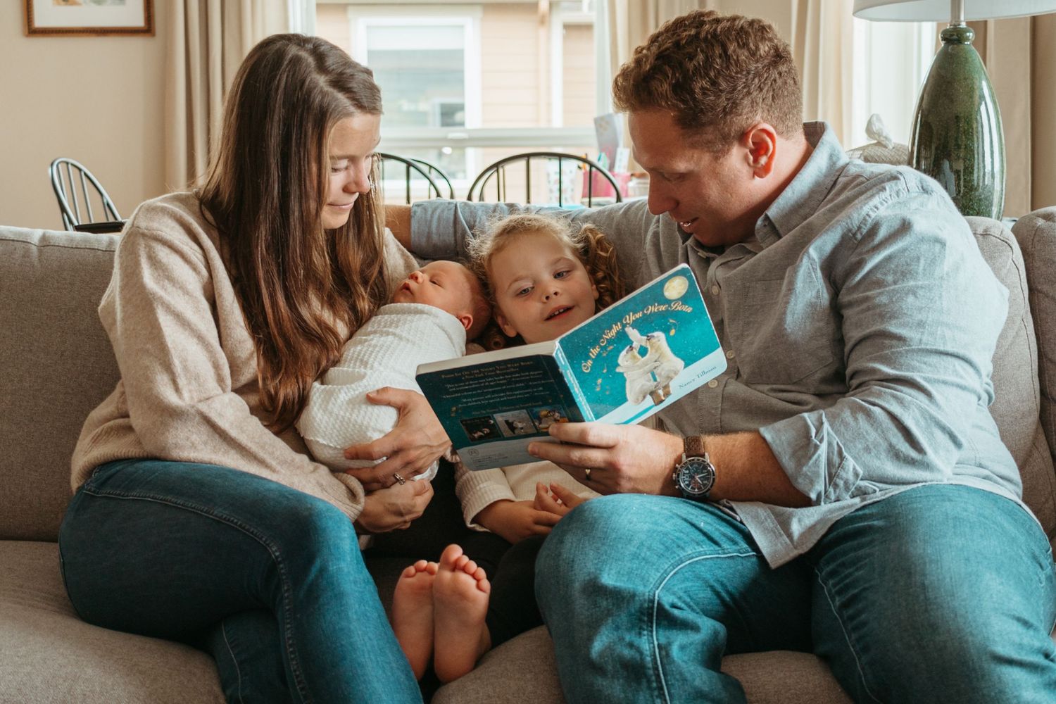 Parents reading a bedtime story to their young child while snuggling together on a couch in a cozy living room.