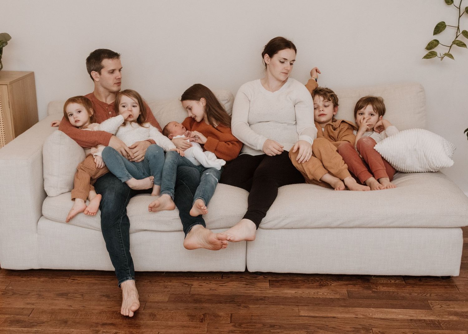 A family relaxes together on a white couch in a minimalist living room with natural lighting.