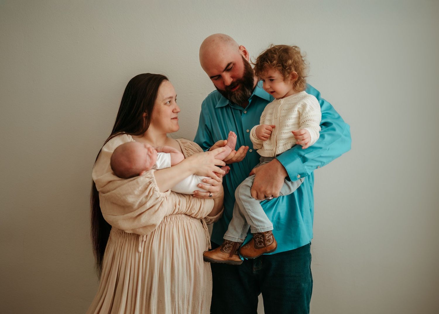 A family wearing beige and turquoise clothing poses together in a studio for portrait photographs.
