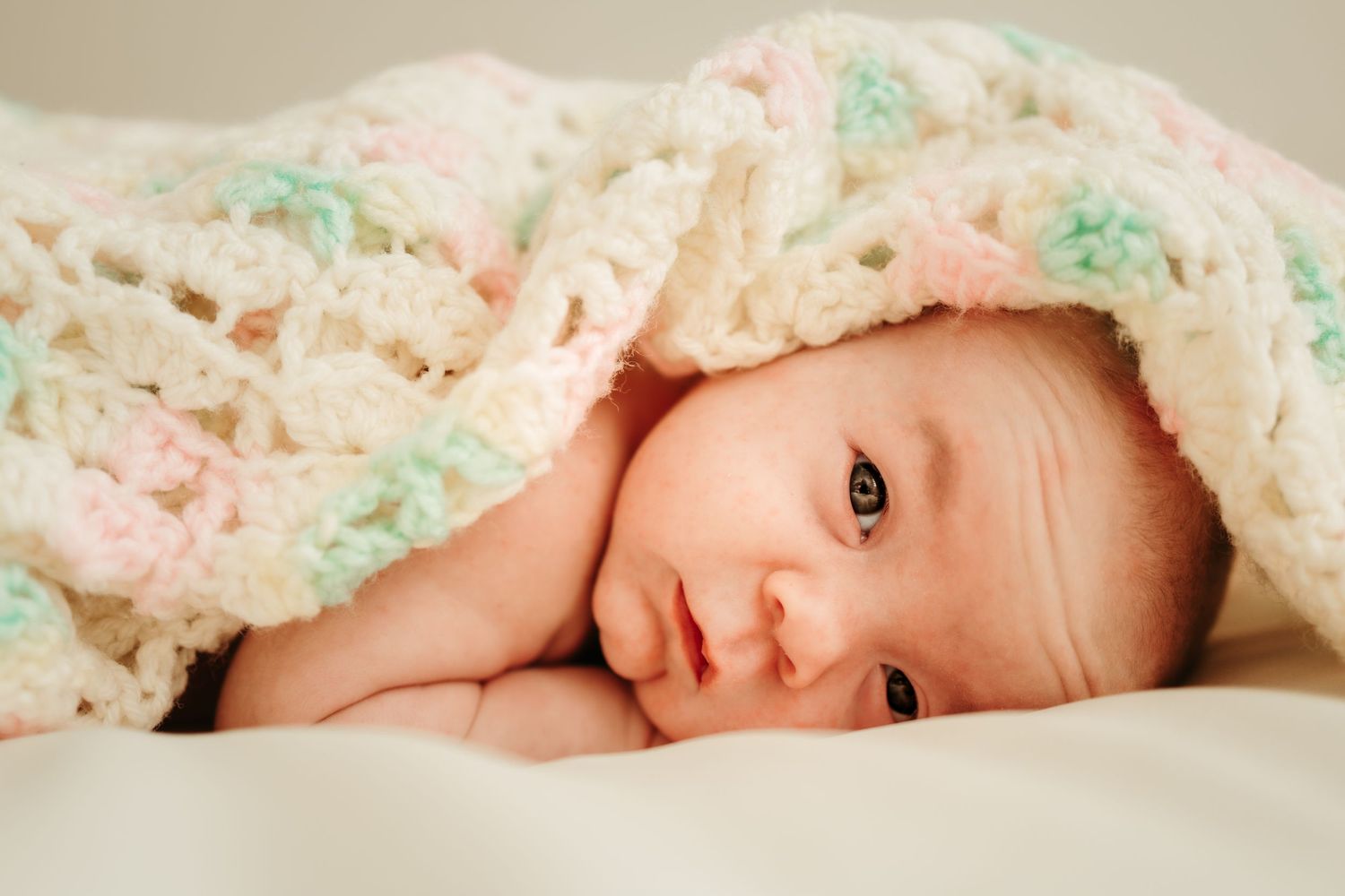 Baby wrapped in floral blanket lying on light colored bedding.