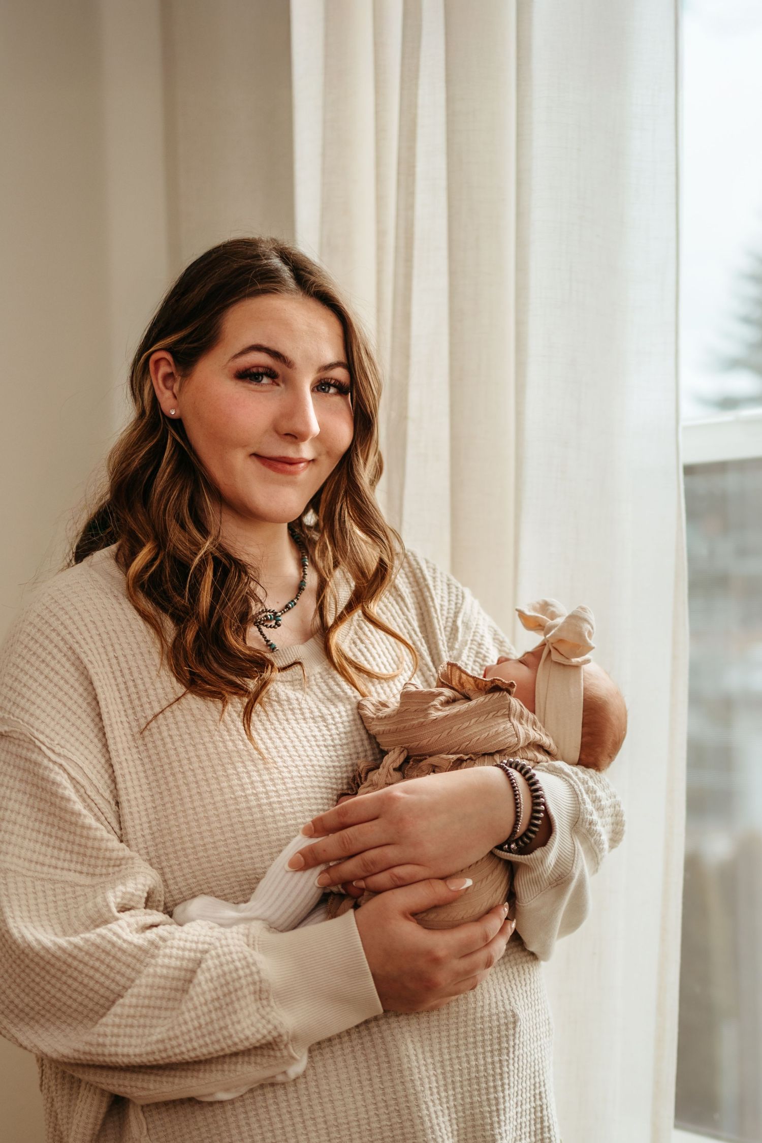A person in a cream knit sweater holds and pets a content ginger cat near a bright window.