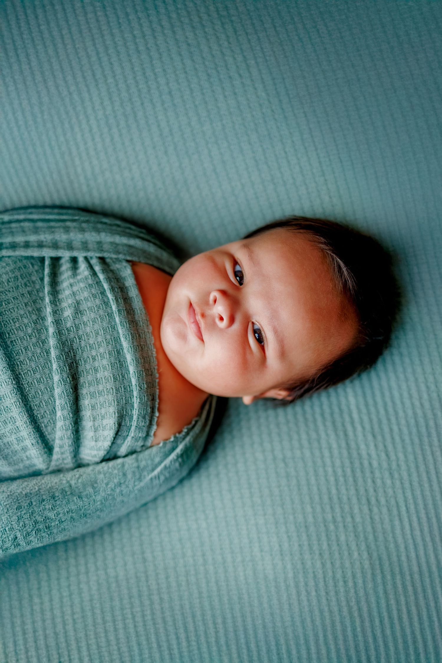 A baby in a gray striped outfit rests on a teal colored textured surface.