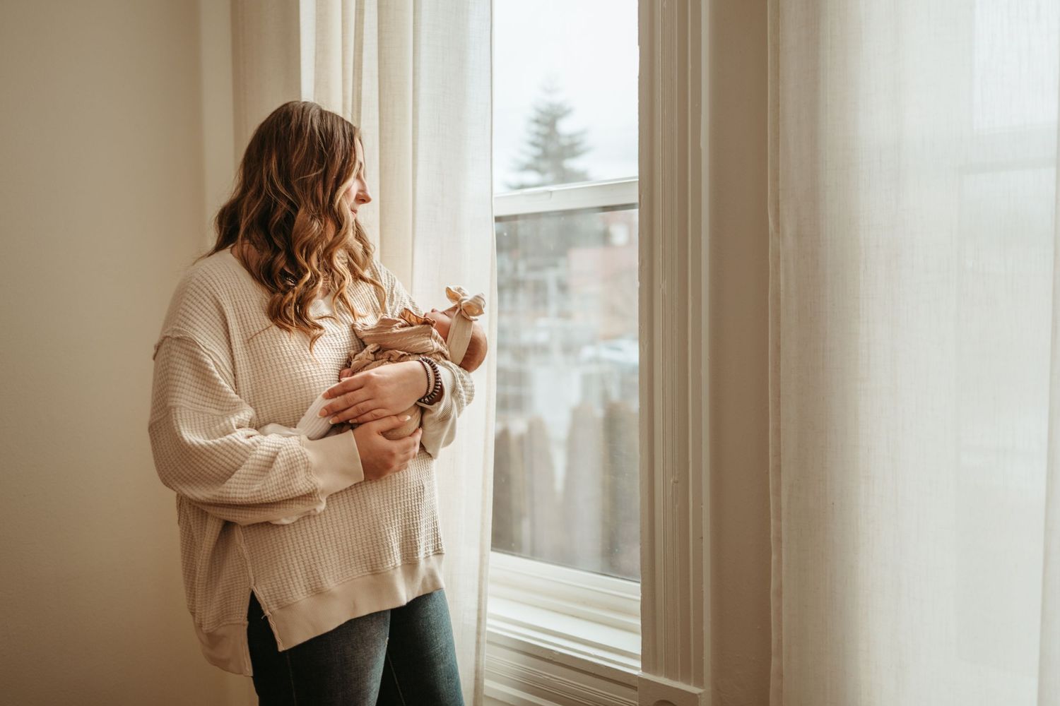 A tender moment between parent and baby captured in warm natural window light with soft neutral tones.