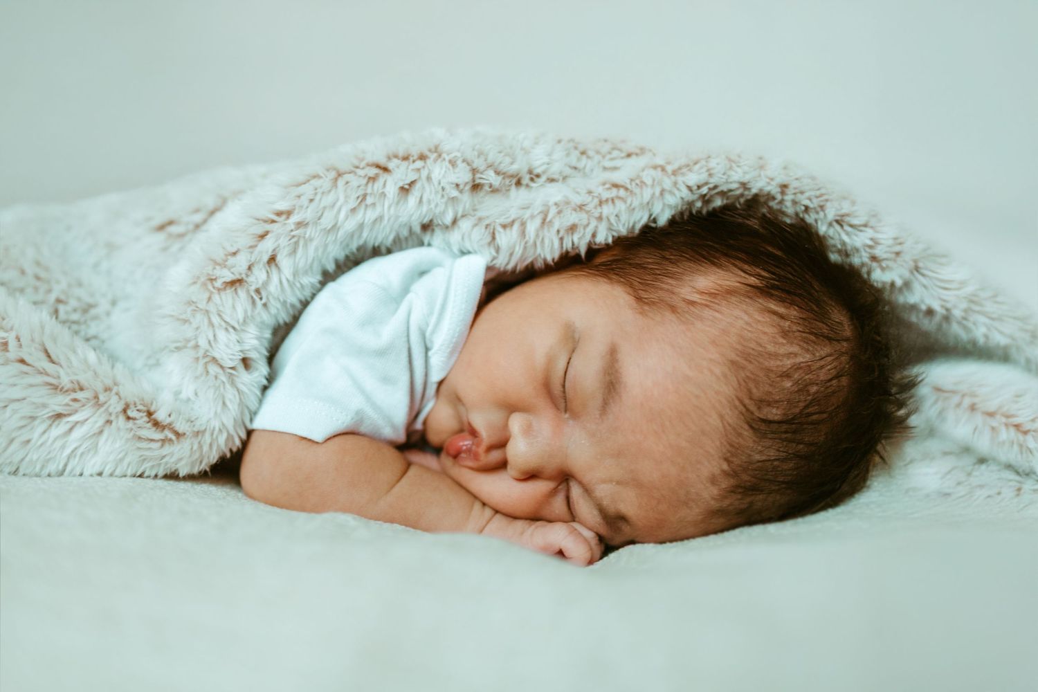 Newborn baby sleeping peacefully on soft white textured blanket in a collection of similar posed photos.