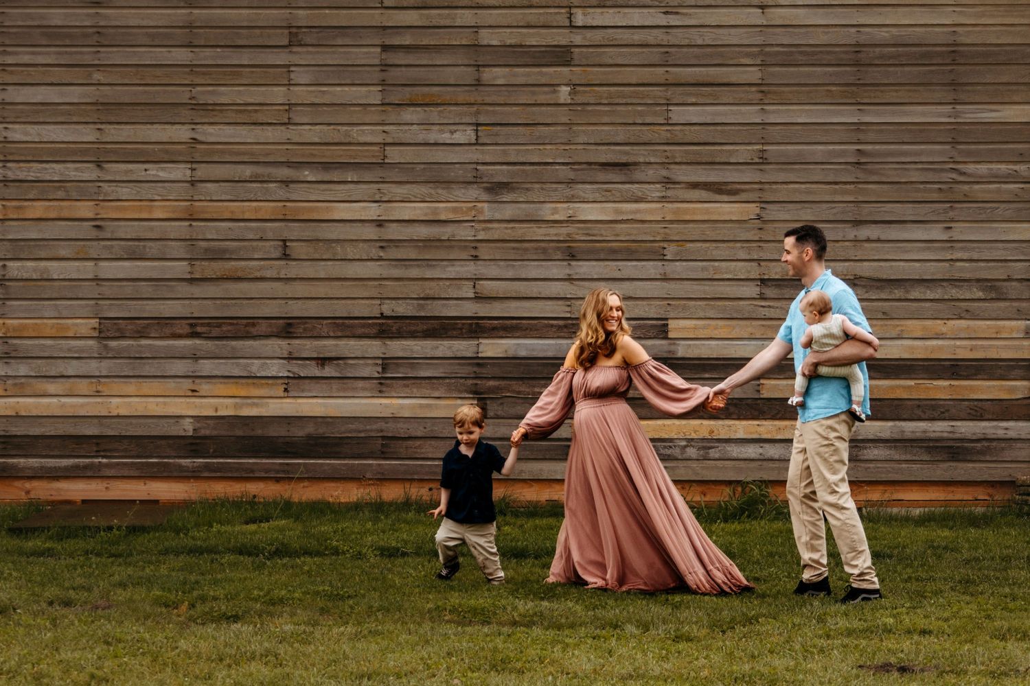 A couple playfully runs and dances together in front of a rustic wooden wall during a photo session.
