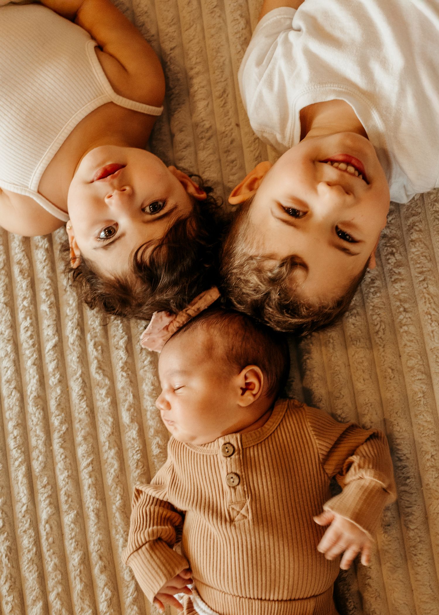 Baby wearing brown knit sweater lies on beige carpet creating mirrored reflection effect in playful composition.