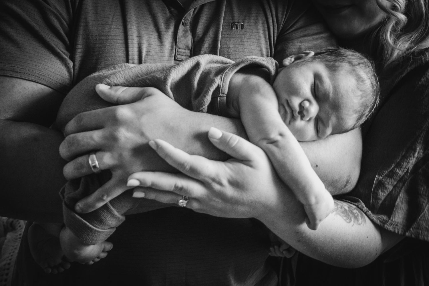 A newborn baby sleeps peacefully while being cradled in protective arms in this intimate black and white photograph.