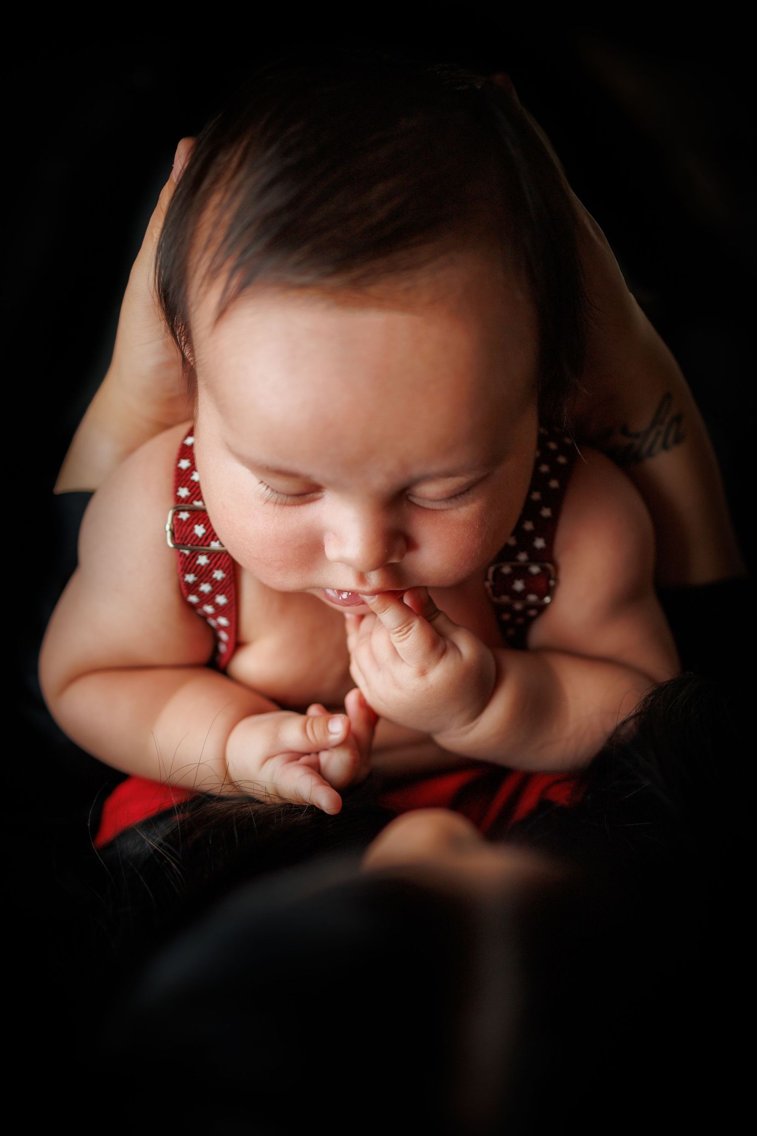 Close-up portrait of infant wearing polka dot red outfit against black background.