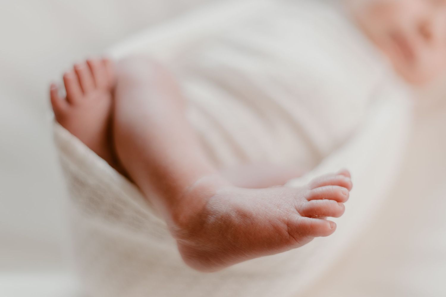 Seven baby feet in a row lay delicately on white bedding, creating a sweet progression of newborn toes.