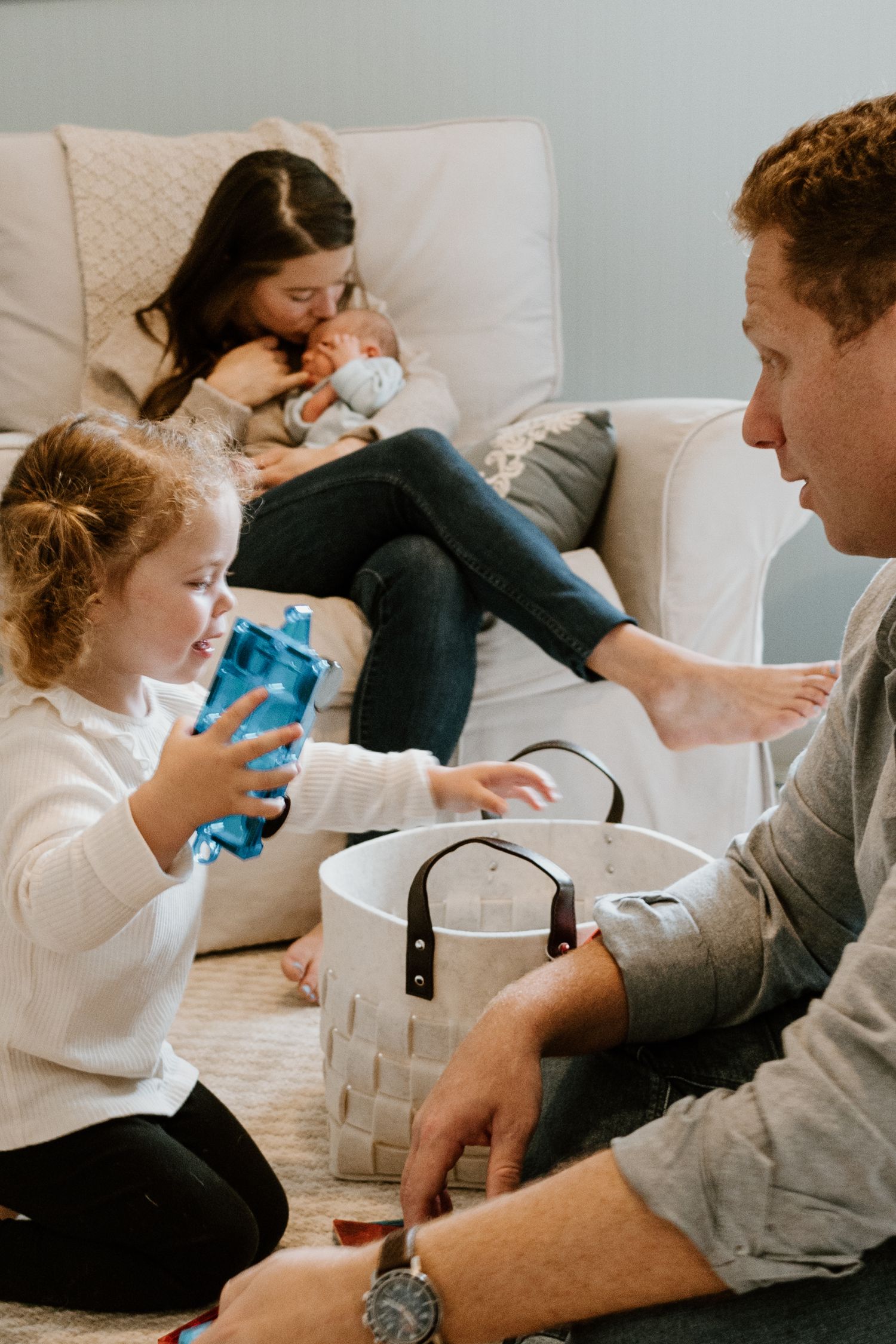 Family relaxes together on a white couch while holding drinks and spending quality time at home.