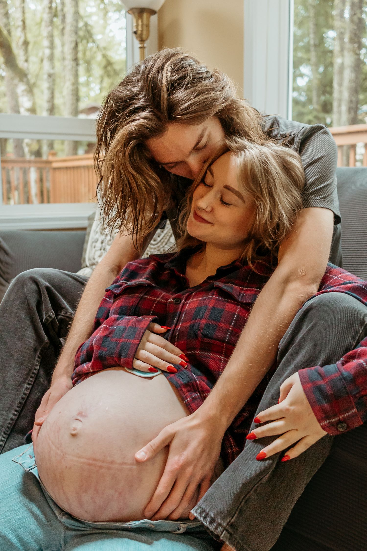 Intimate maternity moment captured as couple cuddles on couch by window.