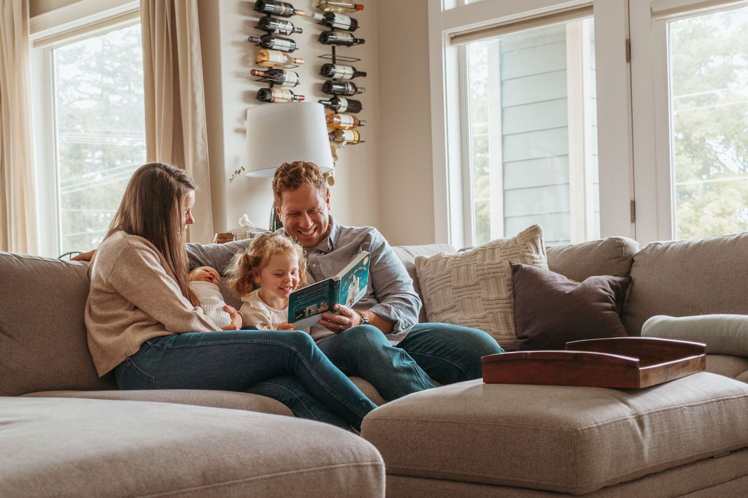 A relaxed family moment on a comfortable gray sectional sofa in a bright living room with natural lighting.