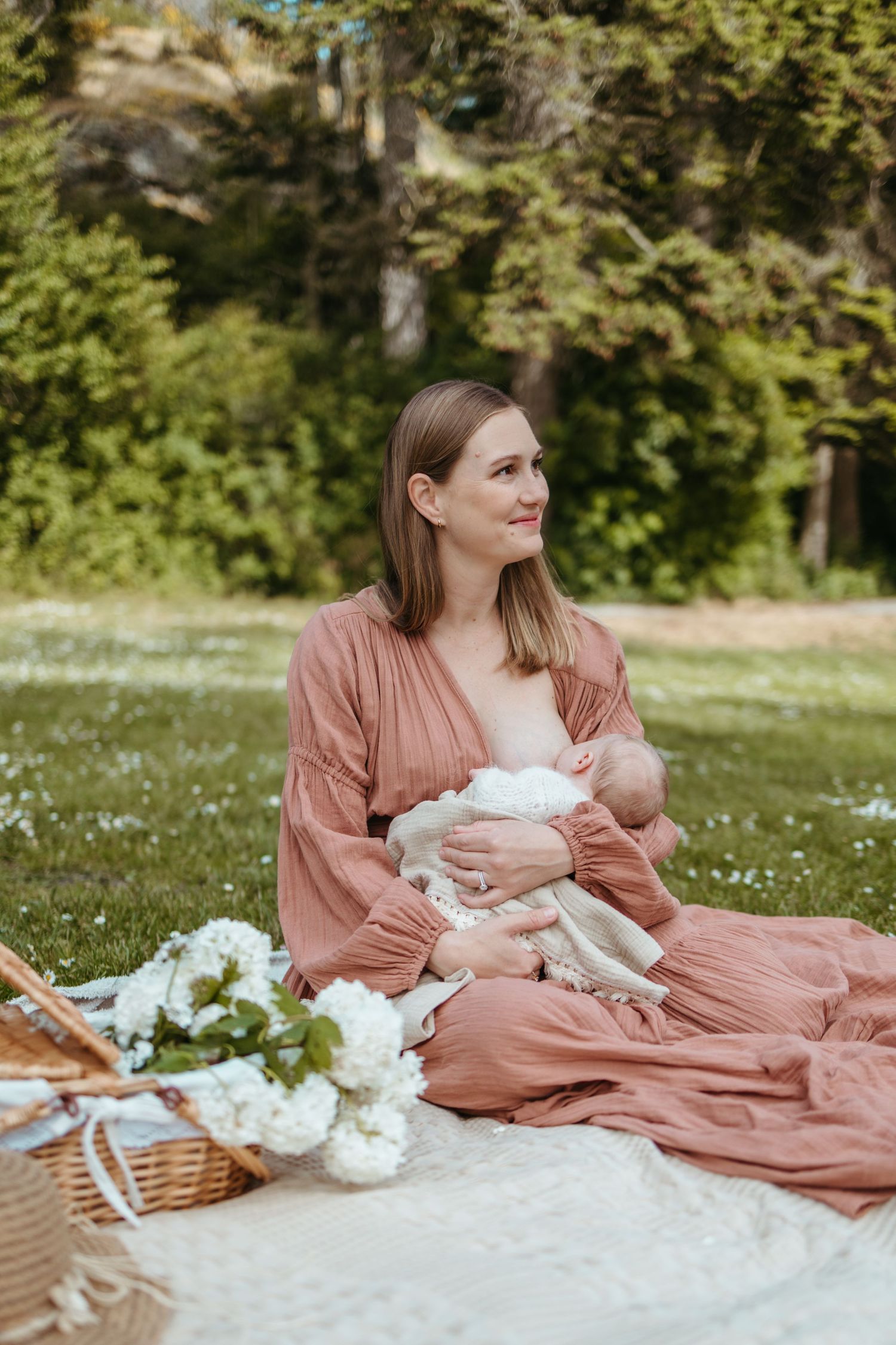 A picnic scene on a blanket with a wicker basket and white flowers in a park on a sunny day.