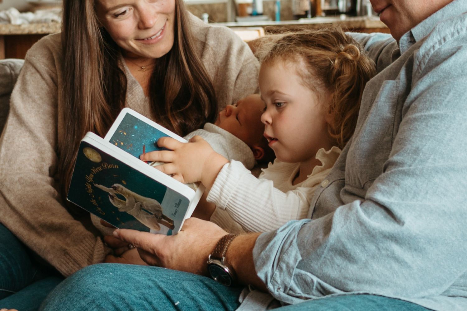 An adult and child reading a book together on a couch while snuggling in a warm, cozy atmosphere.