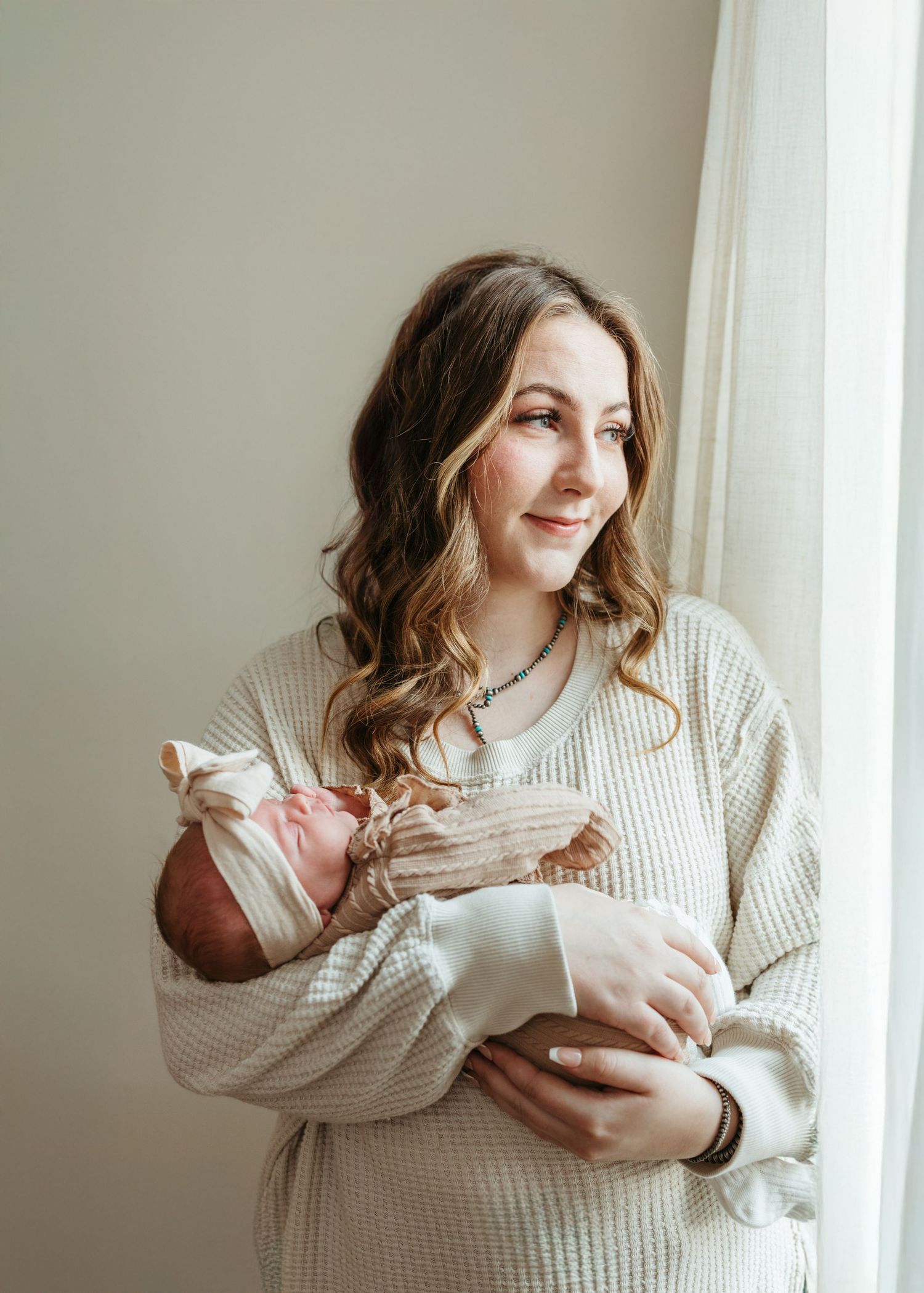 Parent in cream knit sweater holds and feeds newborn baby in intimate indoor portrait session with natural lighting.