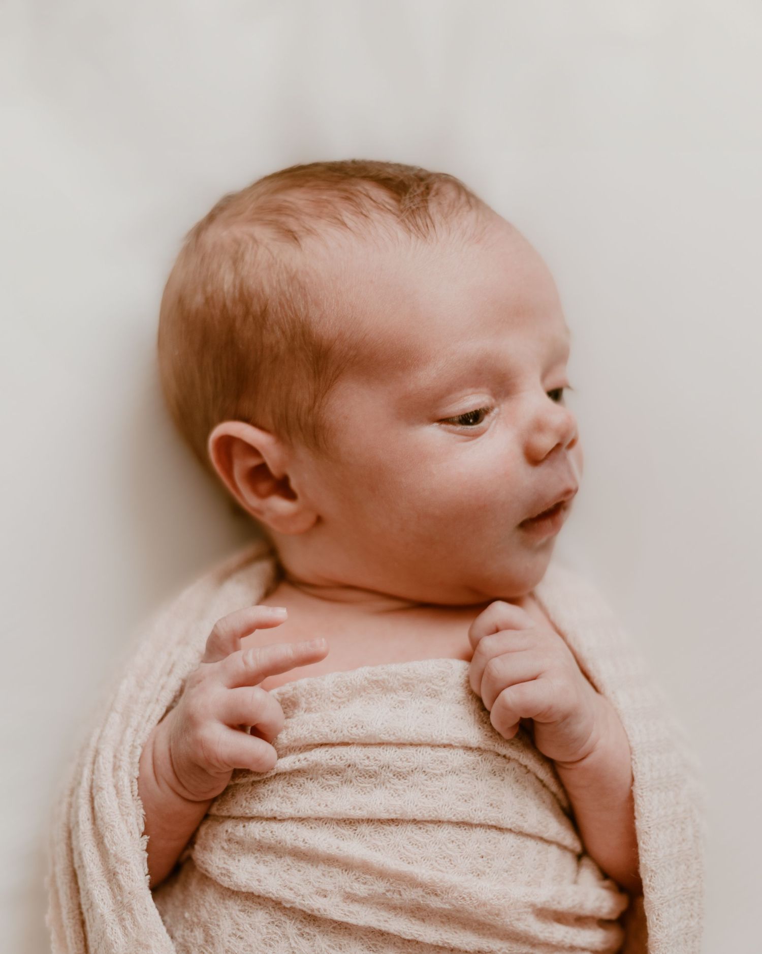 Newborn baby sleeps peacefully on white bedding in progressive profile shots showing gentle face from side angles.