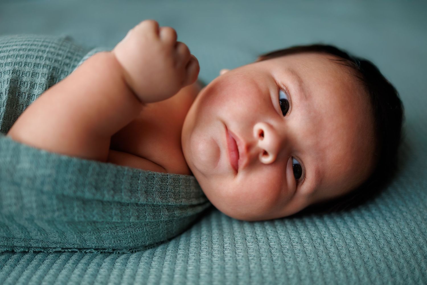 A series of gentle portrait photographs in soft teal tones showing peaceful resting poses on textured fabric.