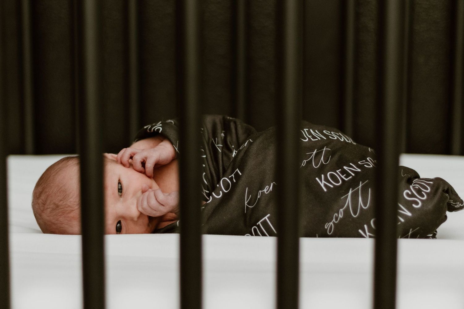 Baby sleeps peacefully in white crib with black text designs visible on the crib rails.