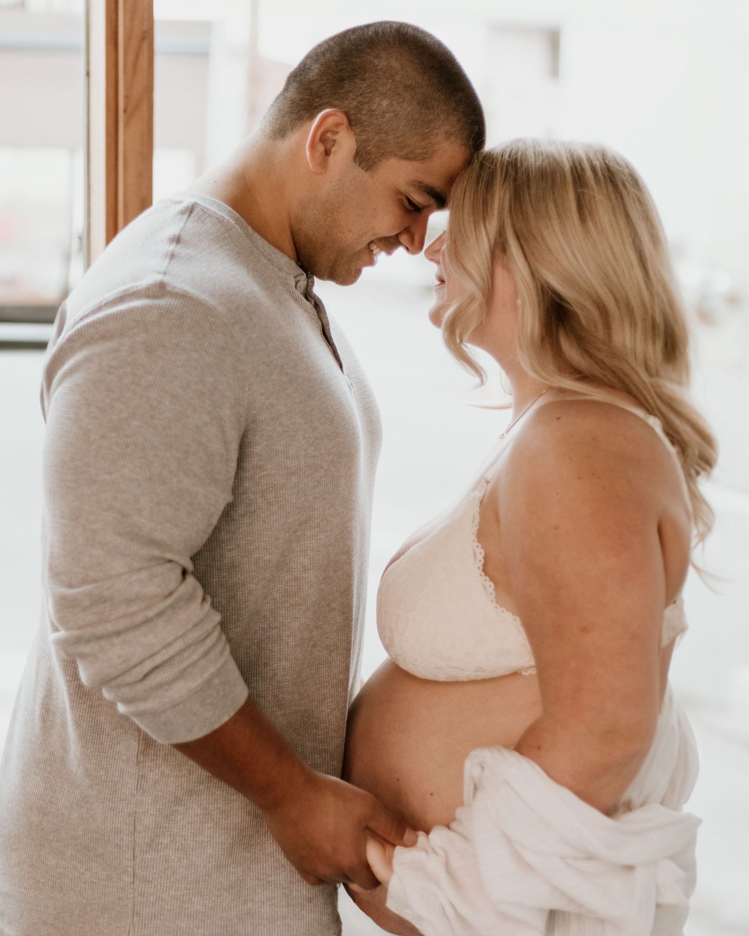 An intimate maternity portrait of a couple in neutral clothing sharing a tender moment.