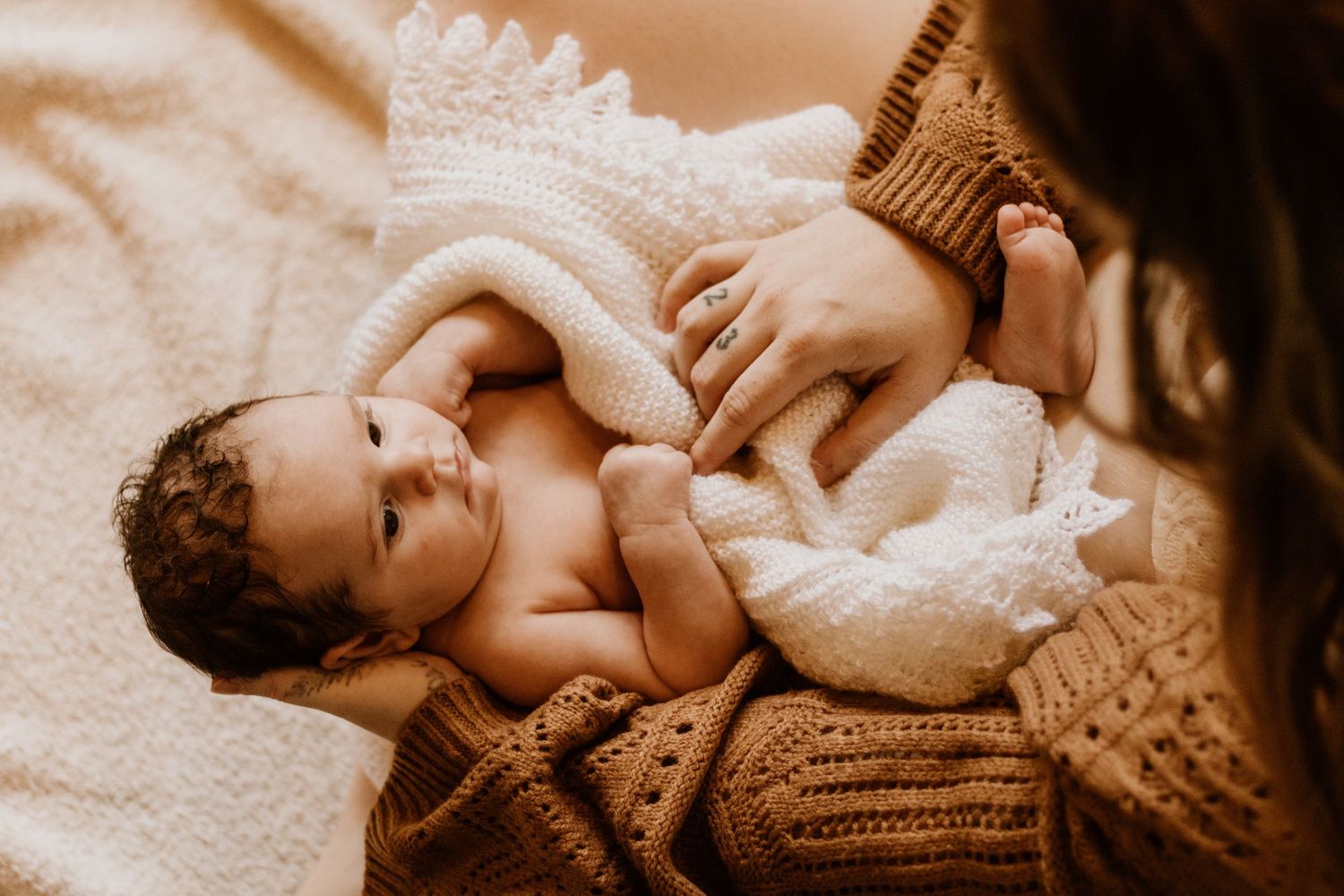 A tender black and white collage of parent and baby moments, showing gentle embraces and loving touches on a soft blanket.