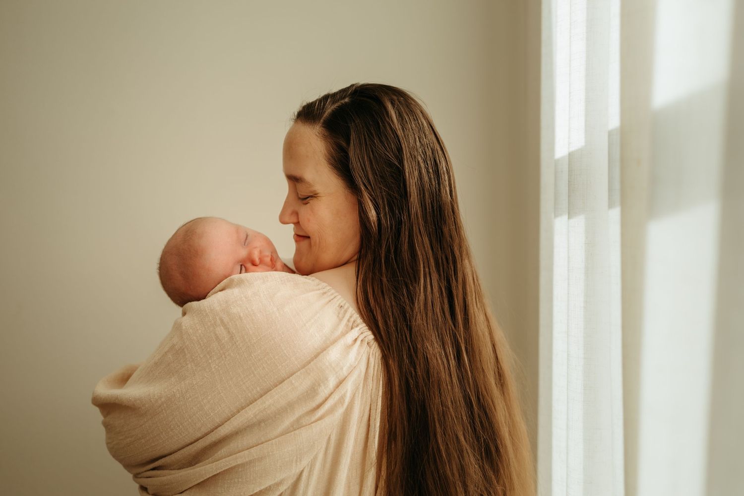 A tender moment between parent and baby by a bright window featuring soft neutral colors and natural lighting.