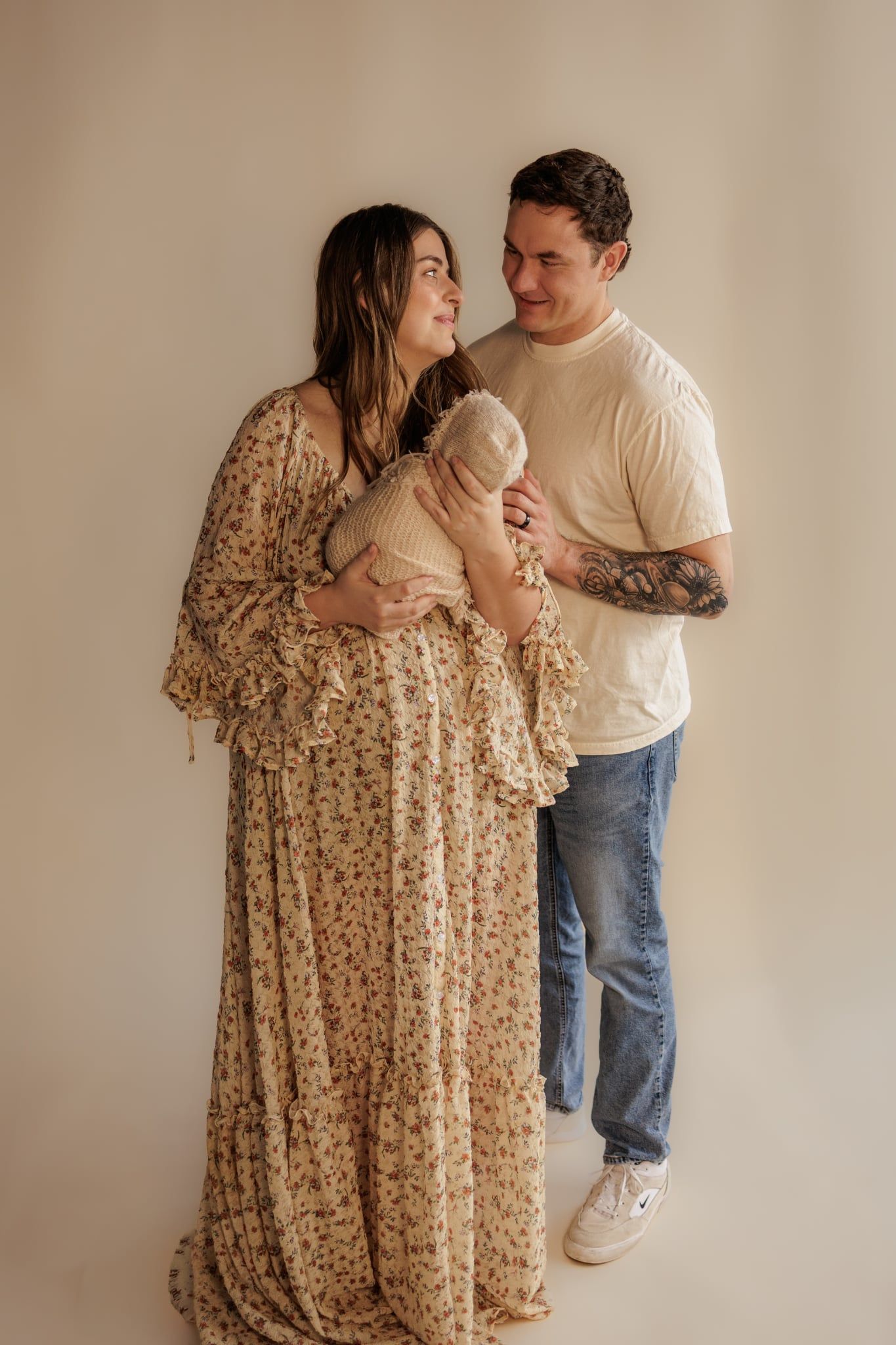 Expecting couple in neutral tones holding newborn baby during a studio maternity photoshoot.