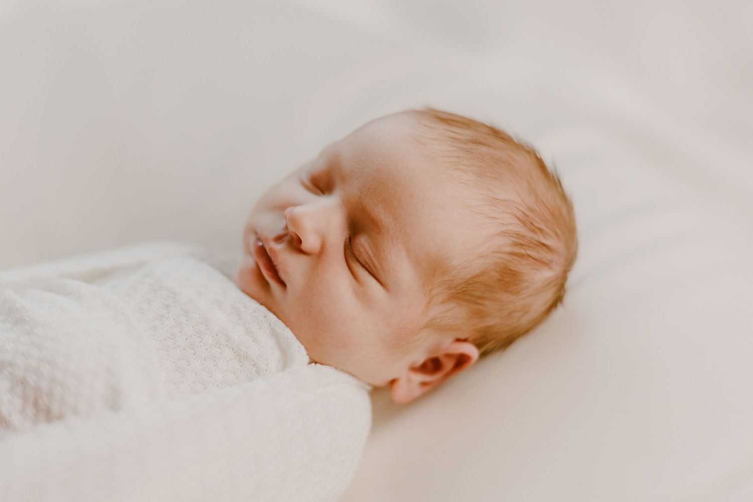 A tiny sleeping baby wrapped in soft white blankets rests peacefully in serene natural lighting.