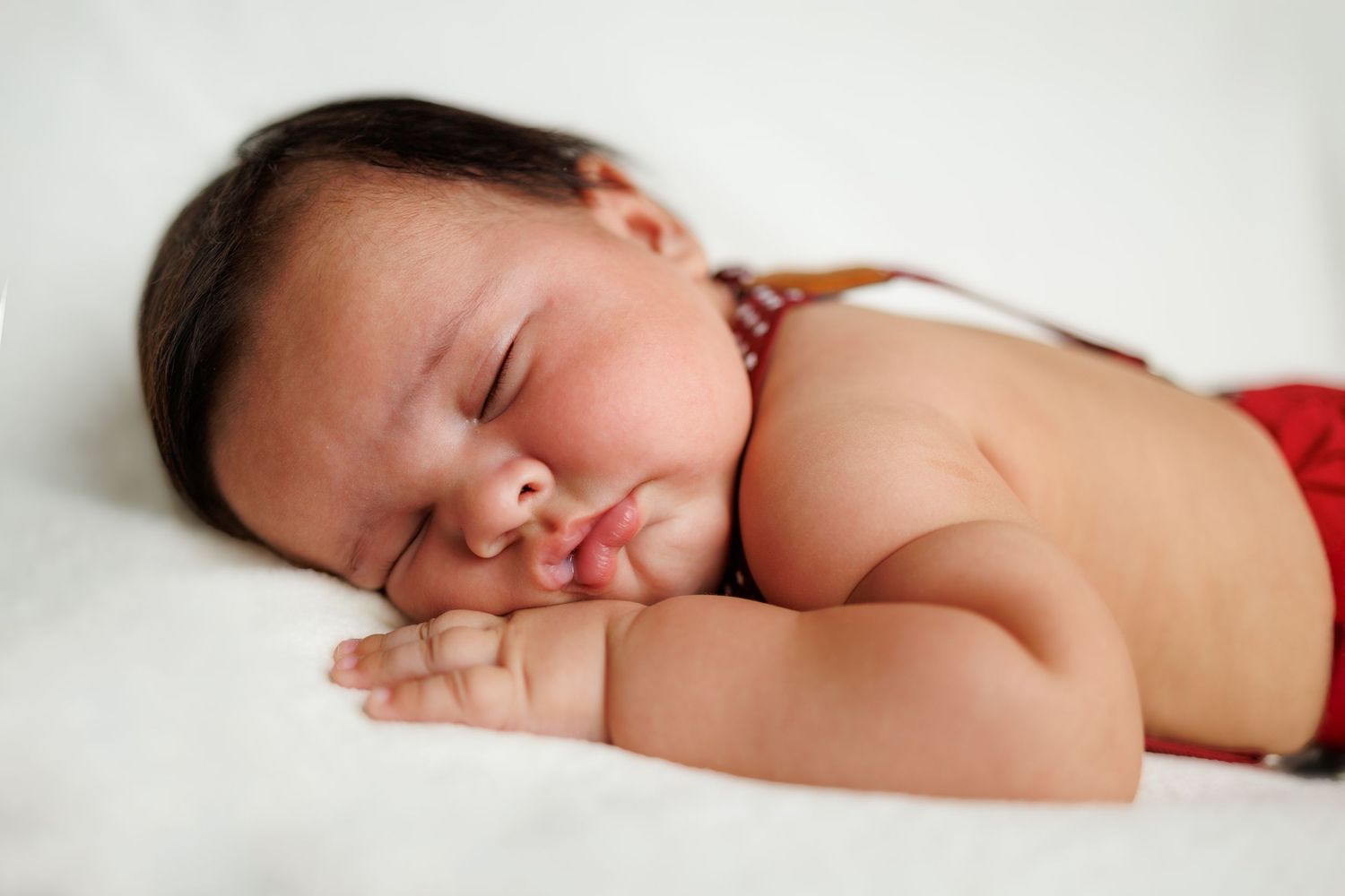 Peaceful sleeping newborn baby rests on soft white blanket in serene natural light.