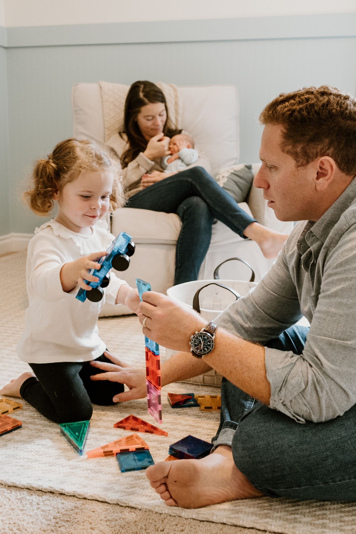 People lying on a white carpet playing with toy cars together in a living room setting.