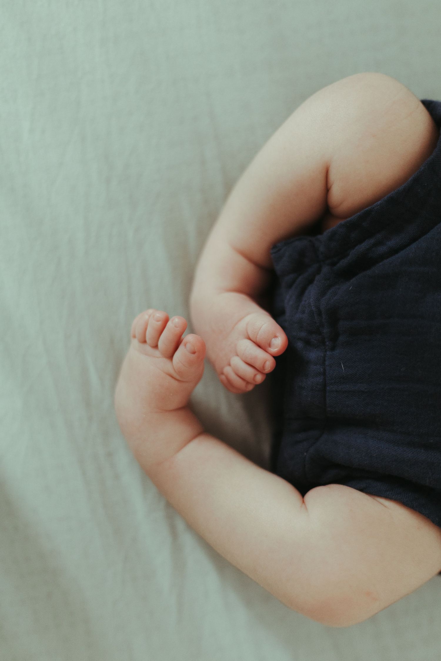 Close-up photo of a sleeping baby's bare arm against a light colored background showing soft skin and tiny fingers.